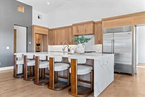 Kitchen with high vaulted ceiling, stainless steel built in fridge, light stone countertops, a breakfast bar, and backsplash