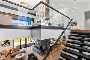 Living area featuring a high ceiling, stairway, a premium fireplace, a chandelier, and finished concrete floors