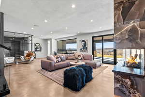 Living room with concrete flooring, a textured ceiling, recessed lighting, and a multi sided fireplace