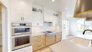 Kitchen featuring appliances with stainless steel finishes, glass insert cabinets, white cabinets, premium range hood, and recessed lighting