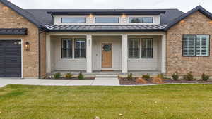 View of front of house featuring a standing seam roof, a porch, brick siding, and a front lawn