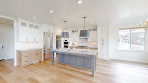 Kitchen with glass insert cabinets, stainless steel appliances, white cabinets, an island with sink, and recessed lighting