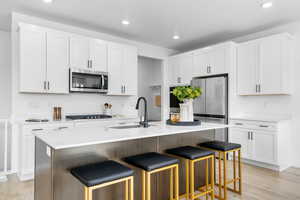 Kitchen with an island with sink, white cabinetry, a breakfast bar area, appliances with stainless steel finishes, and recessed lighting