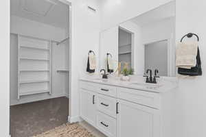 Bathroom with light colored carpet, double vanity, and a spacious closet