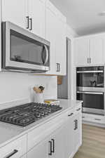 Kitchen featuring appliances with stainless steel finishes, white cabinets, a textured ceiling, and light wood-style flooring