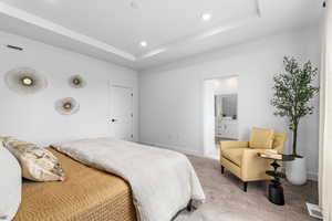 Carpeted bedroom with connected bathroom, a tray ceiling, and recessed lighting