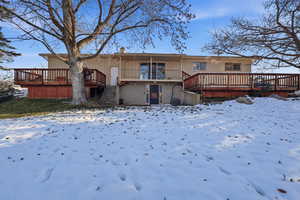Snow covered rear of property featuring brick siding, a deck, a chimney, and stairs