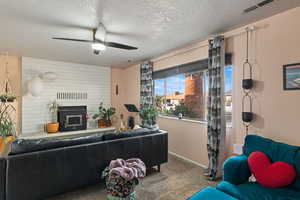 Carpeted living room with a textured ceiling, ceiling fan, and a fireplace with raised hearth