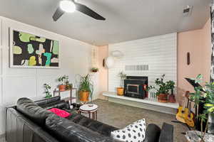 Living area with a decorative wall, a textured ceiling, carpet floors, ceiling fan, and a fireplace