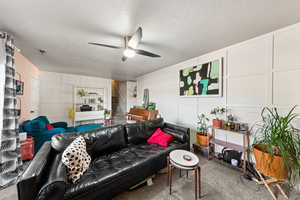Living room featuring a decorative wall, carpet, a textured ceiling, a ceiling fan, and stairs