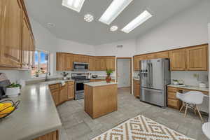 Kitchen featuring stainless steel appliances, light countertops, a kitchen island, high vaulted ceiling, and stone tile flooring