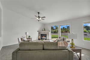 Living area featuring carpet floors, a tiled fireplace, and ceiling fan