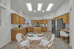 Kitchen with brown cabinetry, appliances with stainless steel finishes, light countertops, high vaulted ceiling, and a kitchen island