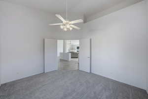 Empty room with high vaulted ceiling, a ceiling fan, and light carpet