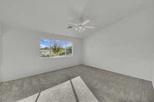 Spare room featuring carpet, vaulted ceiling, and a ceiling fan