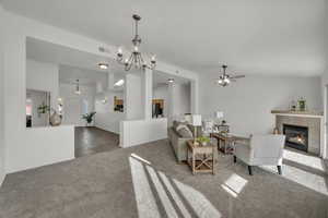 Carpeted living area featuring a chandelier, a fireplace, and a ceiling fan