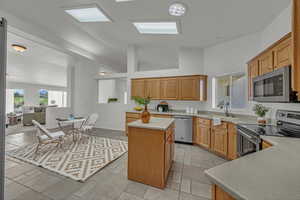 Kitchen featuring appliances with stainless steel finishes, light countertops, a center island, open floor plan, and stone tile floors