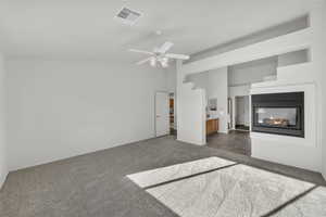 Unfurnished bedroom featuring a multi sided fireplace, connected bathroom, dark colored carpet, and ceiling fan