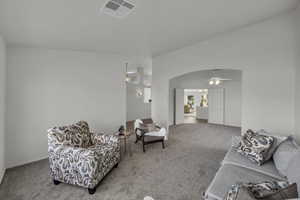 Living area featuring carpet floors, arched walkways, a ceiling fan, and vaulted ceiling