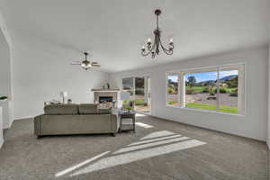 Living room with carpet floors, a tiled fireplace, a chandelier, and ceiling fan