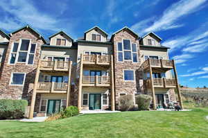 Rear view of property featuring stone siding, a patio area, and a lawn