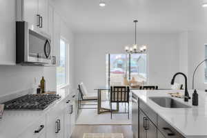 Kitchen featuring stainless steel appliances, light wood finished floors, pendant lighting, light stone counters, and white cabinets