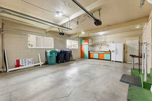 Garage featuring concrete block wall, white fridge with ice dispenser, and separate garage door openers