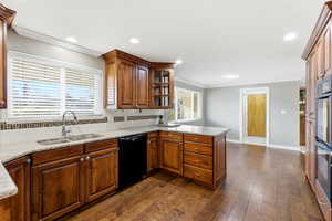 Kitchen featuring a peninsula, light stone counters, black dishwasher, dark wood finished floors, and tasteful backsplash