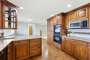 Kitchen featuring brown cabinets, light stone counters, black appliances, a peninsula, and light wood-style floors
