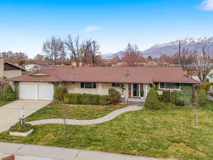 Single story home featuring a mountain view, a front lawn, concrete driveway, an attached garage, and brick siding