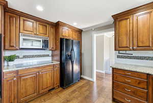 Kitchen with decorative backsplash, black appliances, brown cabinets, light stone counters, and crown molding