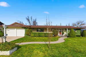 Ranch-style home featuring a front yard, brick siding, an attached garage, and concrete driveway