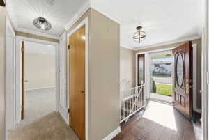 Carpeted entrance foyer with ornamental molding and baseboards