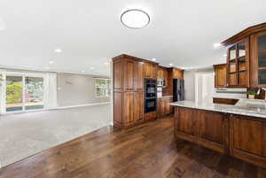 Kitchen with dark colored carpet, open floor plan, light stone countertops, glass insert cabinets, and a peninsula