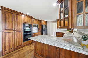 Kitchen with light stone counters, black appliances, brown cabinets, a peninsula, and dark wood finished floors