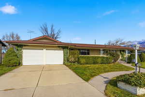 Rambler home featuring an attached garage, driveway, a front lawn, and brick siding