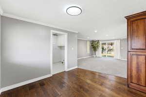 Spare room featuring dark wood-type flooring, ornamental molding, recessed lighting, and dark colored carpet