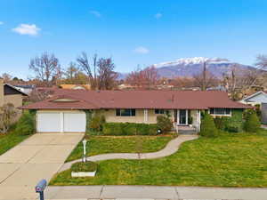 Ranch-style home featuring a mountain view, driveway, a front yard, a garage, and brick siding