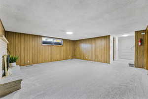 Below grade area featuring wood walls, a brick fireplace, light carpet, and a textured ceiling