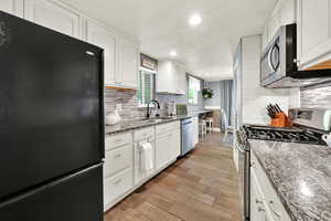 Kitchen with appliances with stainless steel finishes, dark stone counters, recessed lighting, white cabinetry, and wood tiled floors