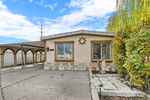 Rear view of property with stucco siding, an attached carport, stone siding, and concrete driveway