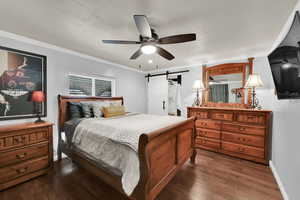 Bedroom with a barn door, ornamental molding, dark wood finished floors, a ceiling fan, and recessed lighting
