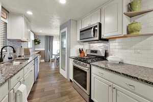 Kitchen featuring stainless steel appliances, open shelves, dark stone countertops, white cabinets, and recessed lighting