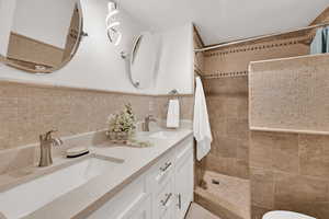 Full bathroom featuring a walk in shower, double vanity, tile walls, and wainscoting