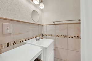Bathroom featuring vanity, a textured wall, tile walls, and a wainscoted wall