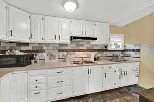 Kitchen with light countertops, white cabinets, decorative backsplash, and under cabinet range hood
