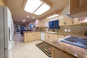 Kitchen featuring white appliances, a peninsula, granite countertops, tasteful backsplash, and light tile patterned floors