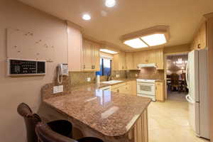 Kitchen featuring a kitchen breakfast bar, white appliances, backsplash, and under cabinet range hood