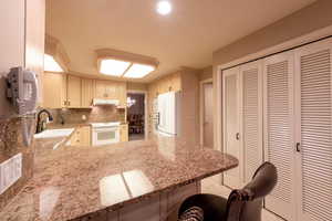 Kitchen featuring white appliances, backsplash, granite counters, and a kitchen breakfast bar