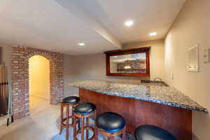 Indoor bar with granite countertops, arched walkways, and light carpet in recreation room
